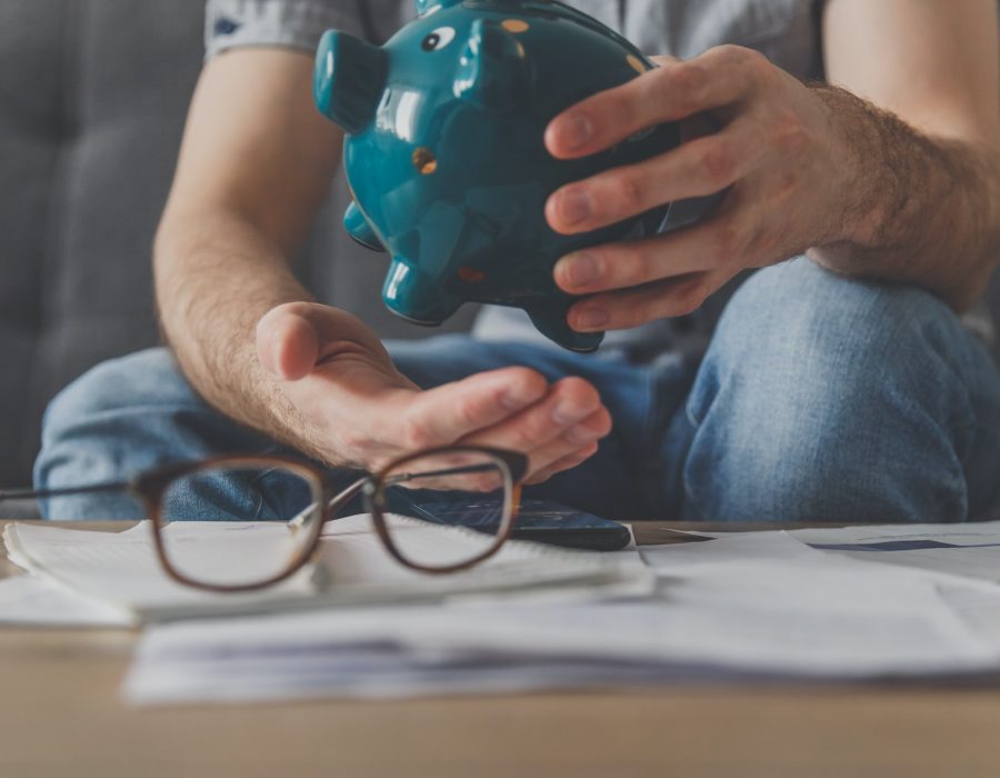 Man sitting at a table full of unpaid bills shakes out the last penny from the piggy bank
